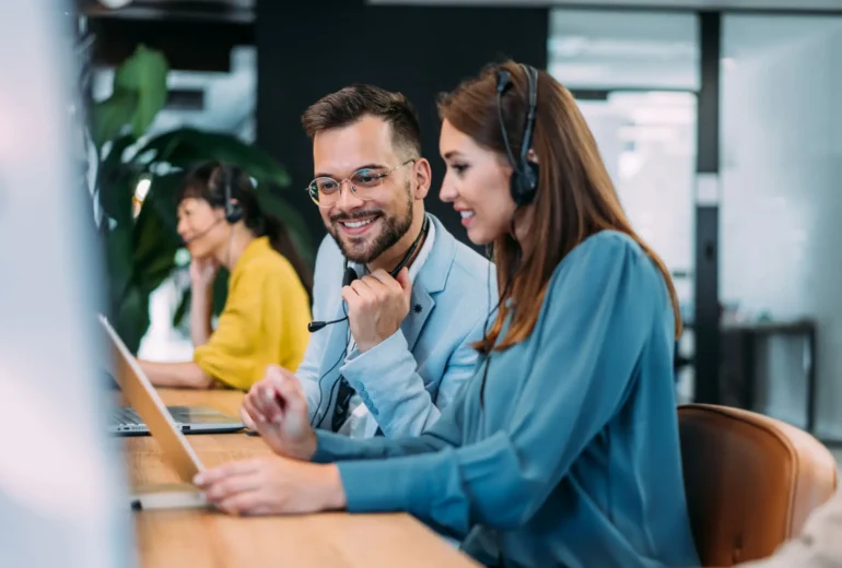 Smiling call center agents collaborating at computers
